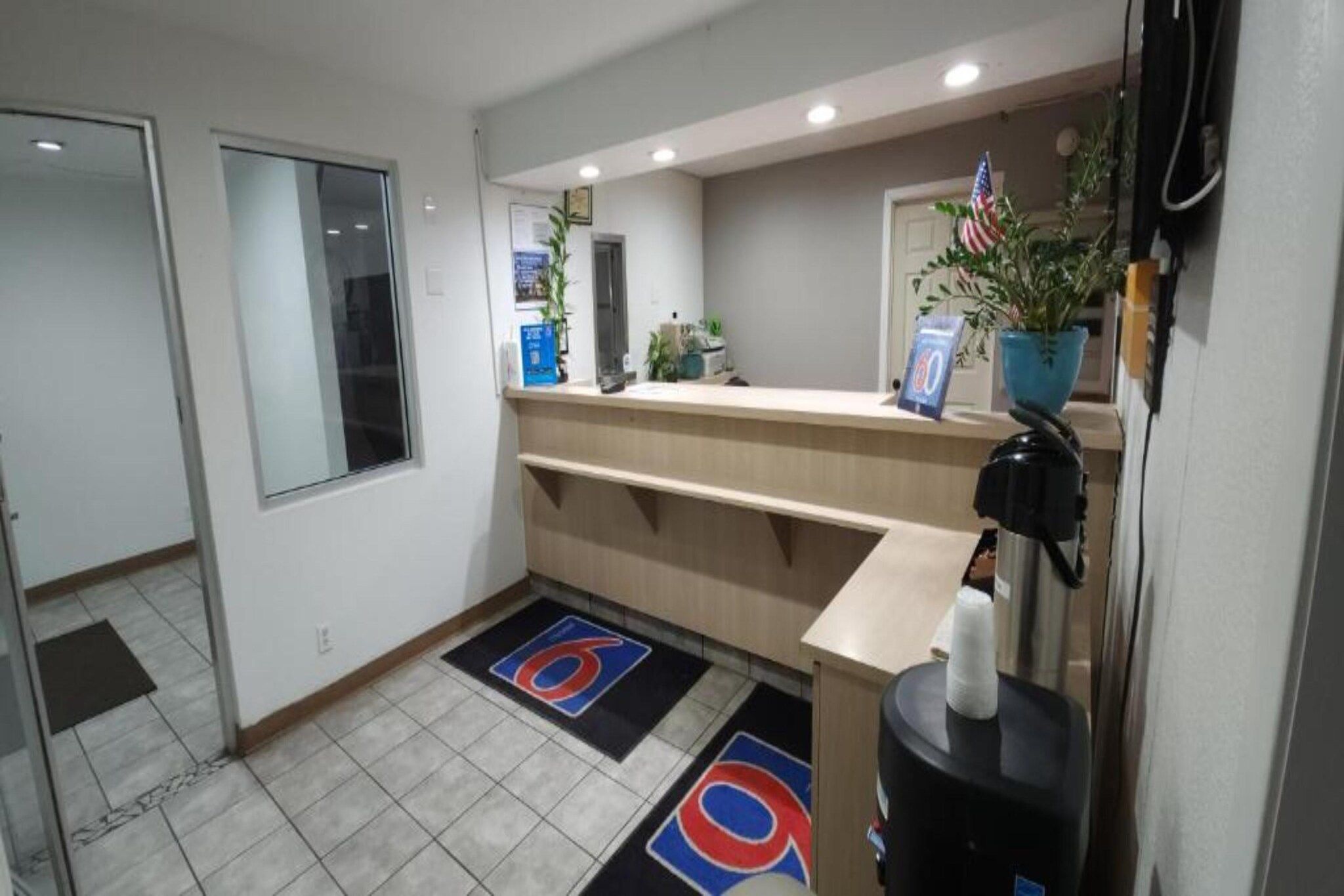 Zona de recepción de un hotel con mostrador, una planta, una bandera y una puerta.