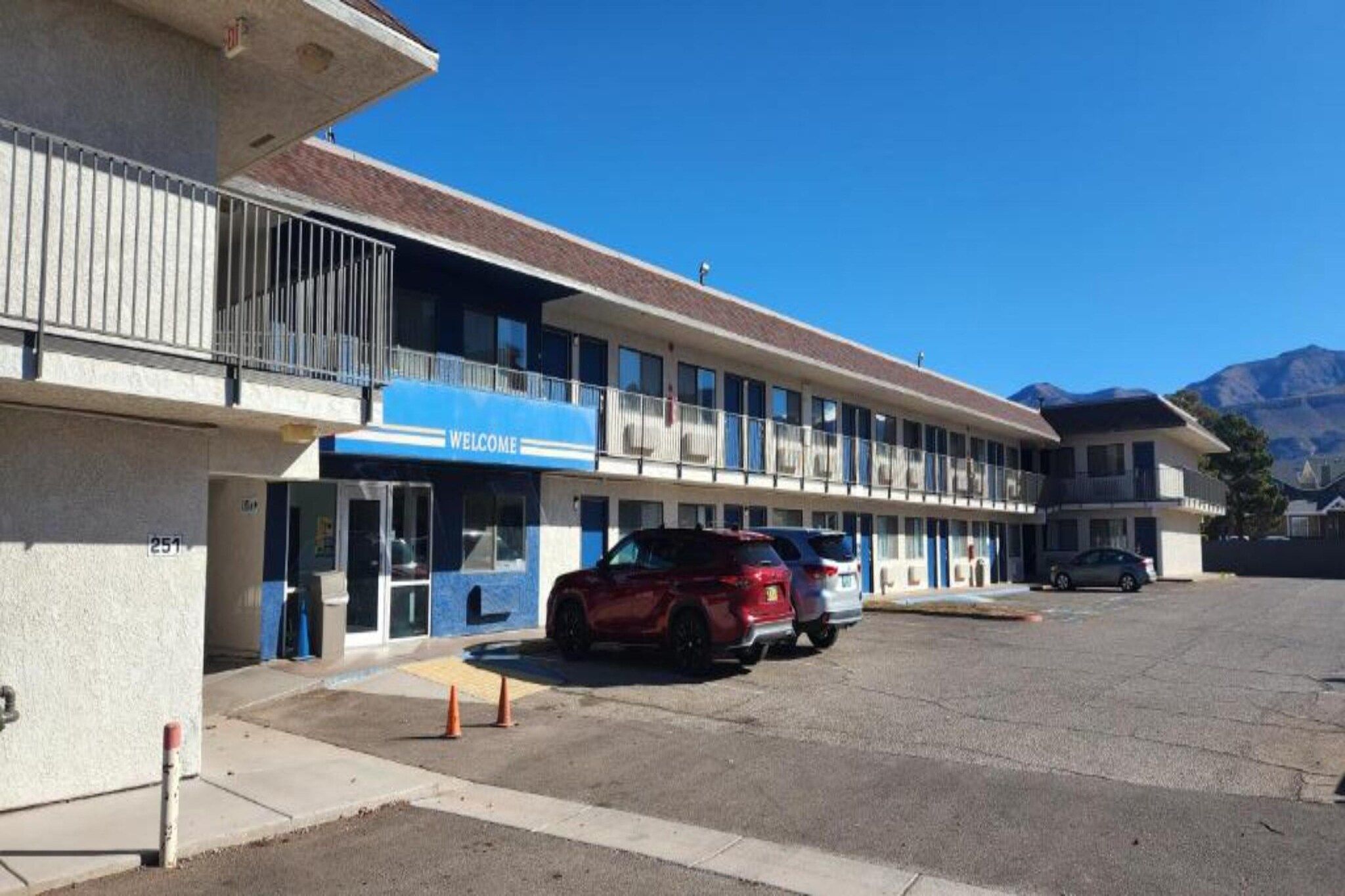 A motel with a 'WELCOME' sign, a parking lot, and a mountain in the background.
