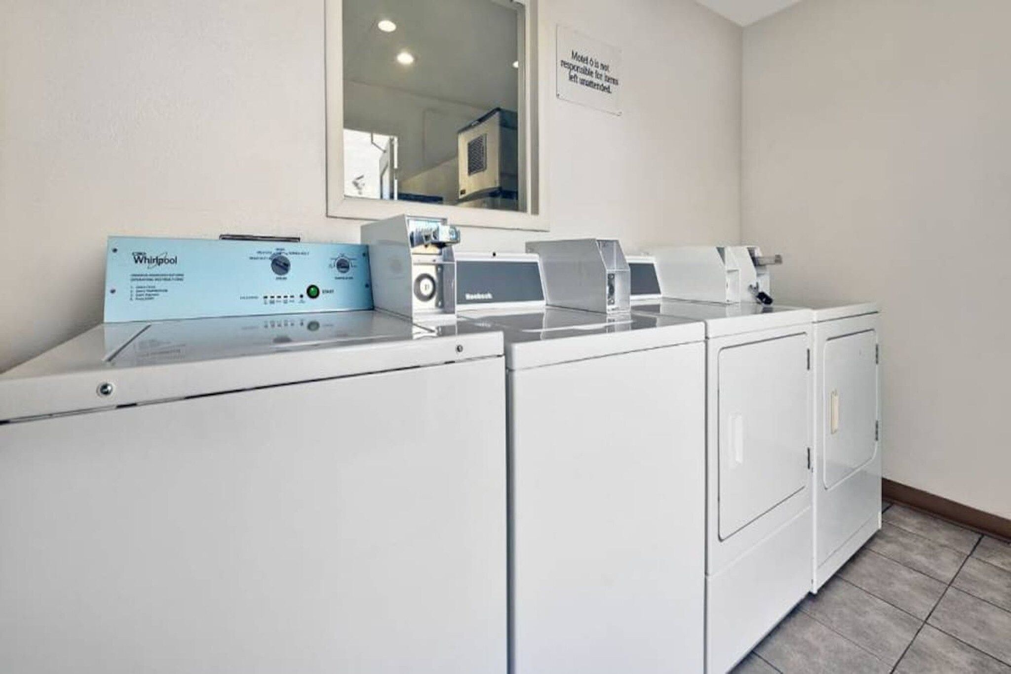 Ett tvättrum med en tvättmaskin och en torktumlare av märket Whirlpool, en spegel och en skylt på väggen.