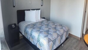 Una habitación de hotel con cama, mesita de noche y lámpara fijada a la pared.