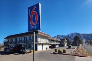 A motel with a prominent '6 ENTER' sign, a parking lot, and a mountain backdrop. - 1 Queen Bed | Non-Smoking, Micfridge (Alamogordo)