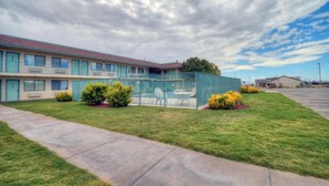 Un motel con un área exterior cercada, un estacionamiento y un edificio con varias ventanas.