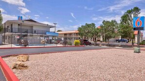 A motel with a fenced parking area, a building with a '6' sign, and a clear sky. - Spacious 2 Full Beds |Motel 6 Gallup, NM (Gallup)