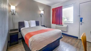 Een hotelkamer met een bed, nachtlampjes, een raam met gordijnen, een airconditioning en een stoel.