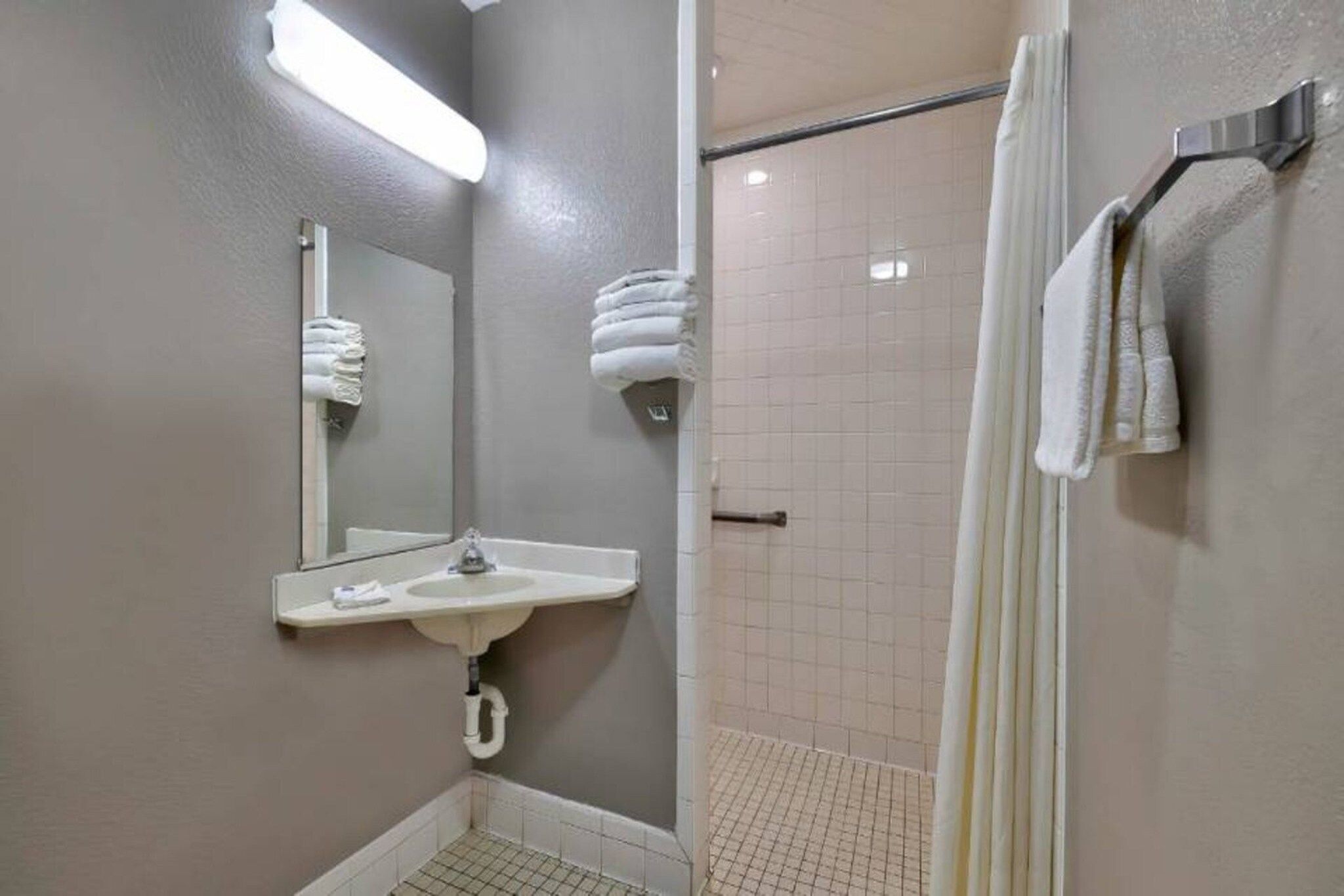 A bathroom with a sink, mirror, towel rack, and shower area.