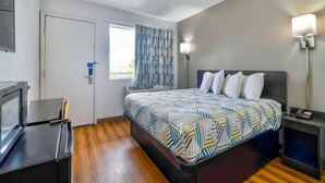Een hotelkamer met een bed, een bureau, een televisie, een raam met gordijnen en een nachtkastje met een lamp.