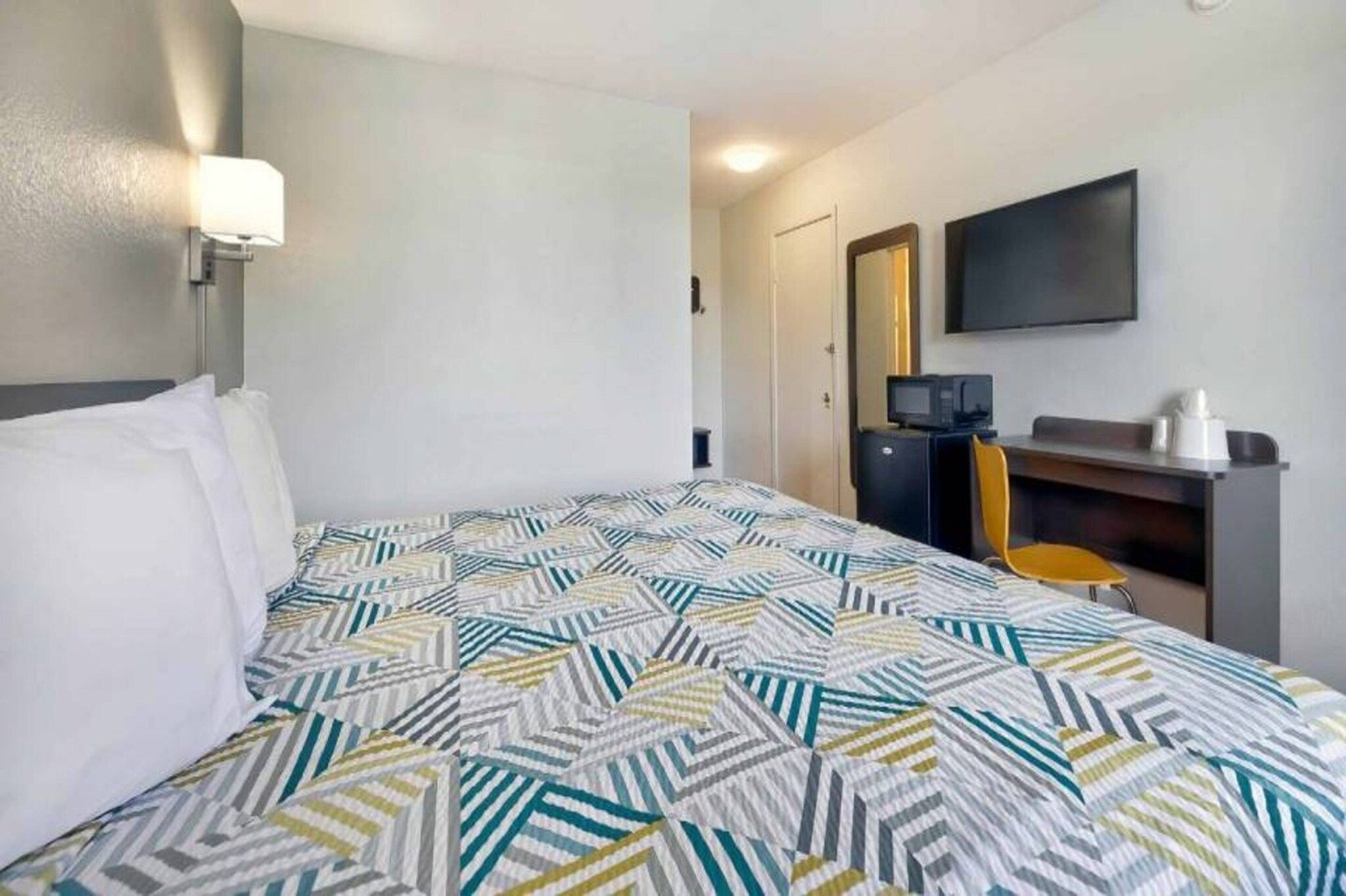 Una habitación de hotel con cama, escritorio, silla, televisor y microondas.