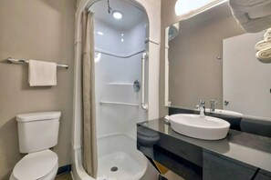 Een badkamer met een douchecabine van glas, een wit toilet, een wastafel met spiegel en een handdoekhouder met een witte handdoek.
