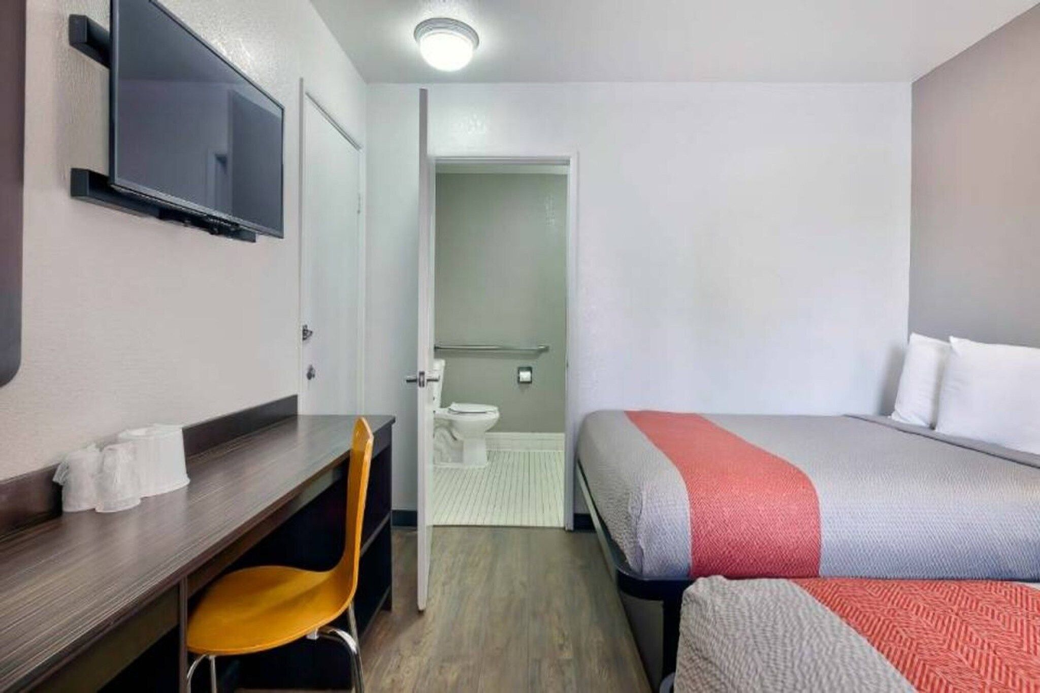 Habitación de hotel con cama, escritorio, silla, televisor y baño visible a través de una puerta abierta.