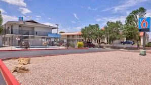A motel with a fenced parking area, a building with a '6' sign, and a clear sky. - 2 Full Beds | Mobility Accessible Tub (Gallup)