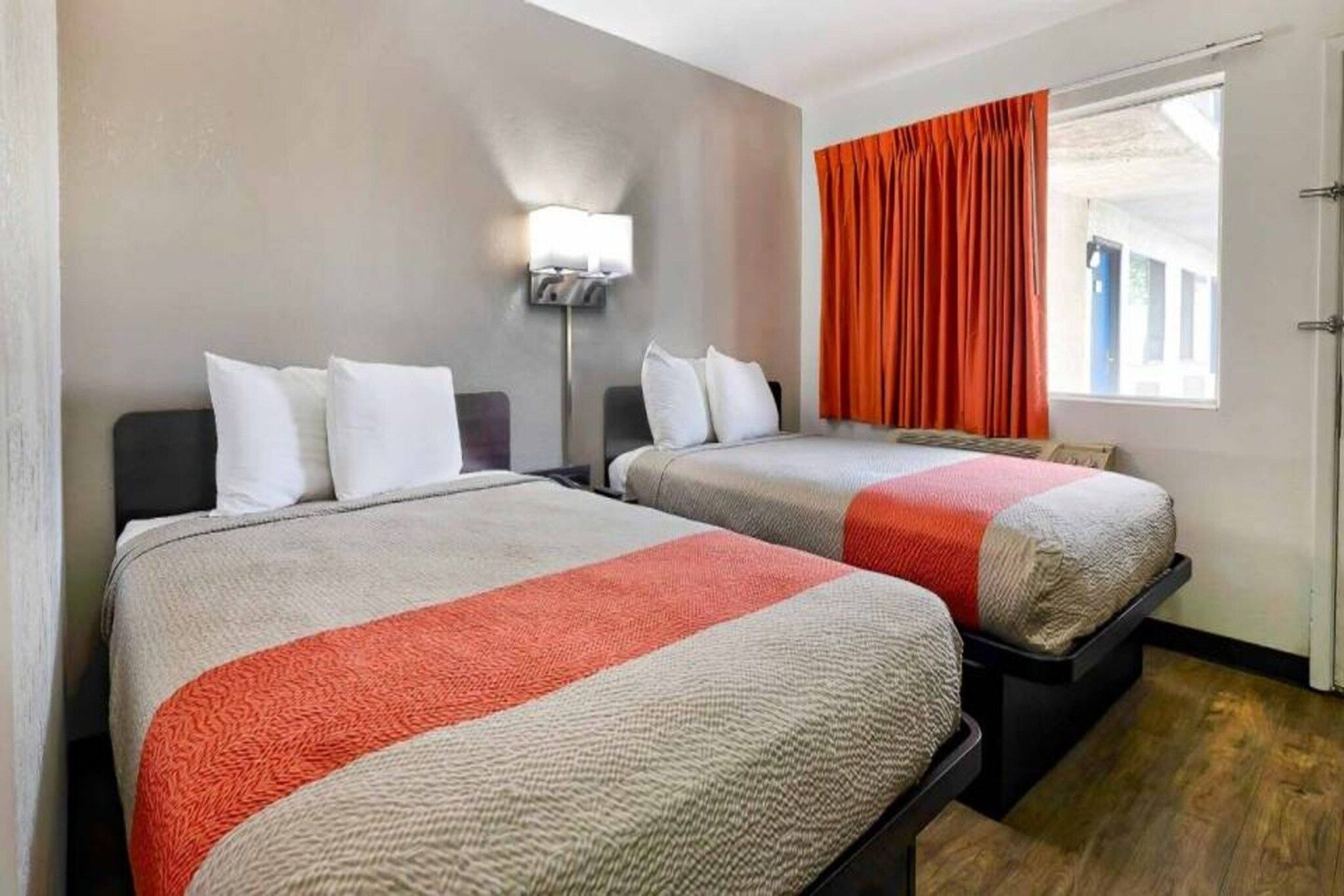 A hotel room with two beds, a nightstand, a lamp, and a window with curtains.
