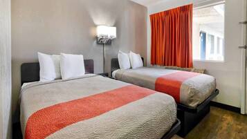 A hotel room with two beds, a nightstand, a lamp, and a window with curtains.