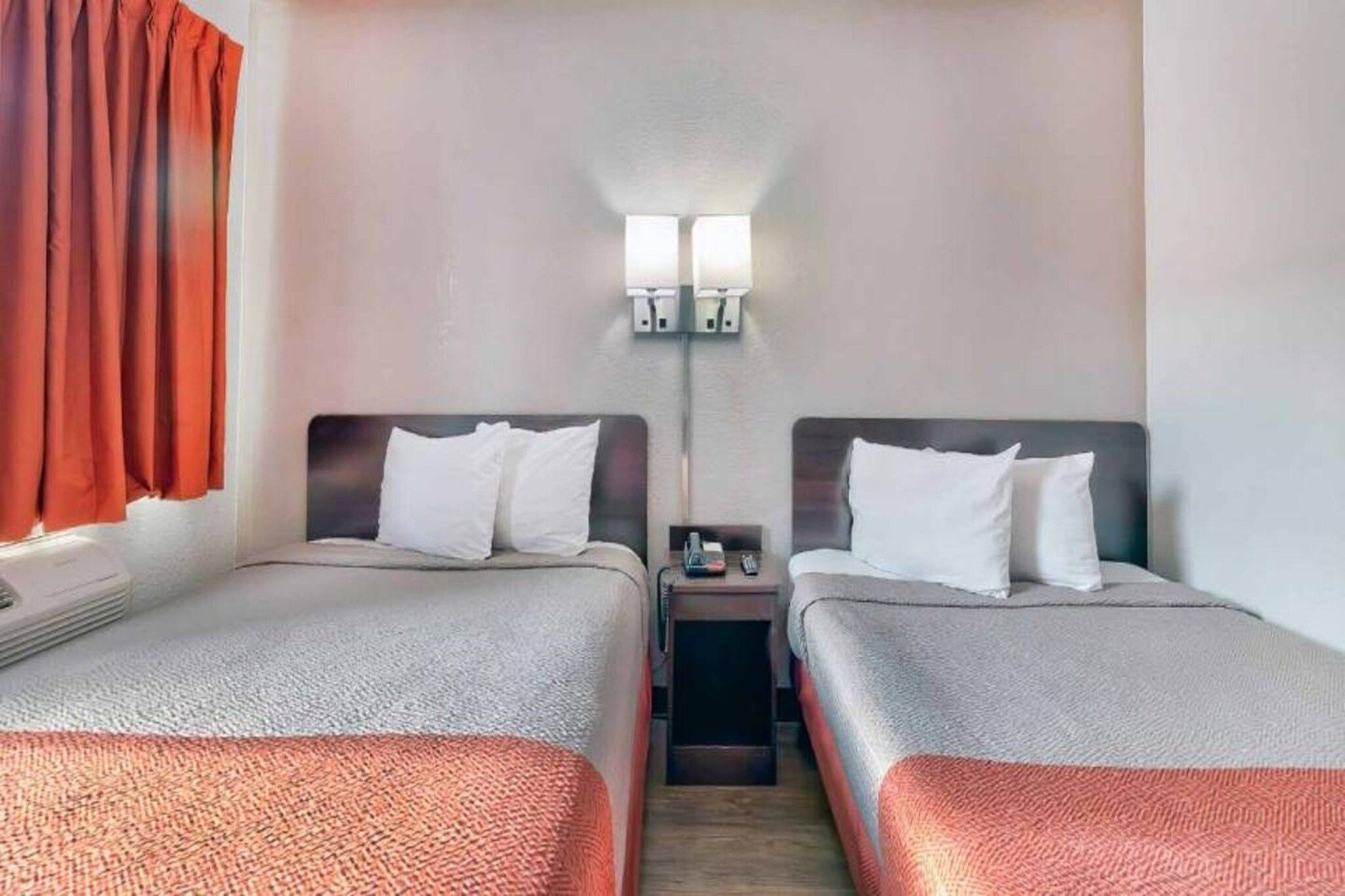 Et hotelværelse med to senge, et natbord, en lampe og et vindue med gardiner.