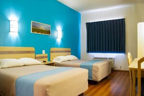 Quarto de hotel com duas camas, uma escrivaninha, uma cadeira, uma janela com cortinas e um quadro na parede.