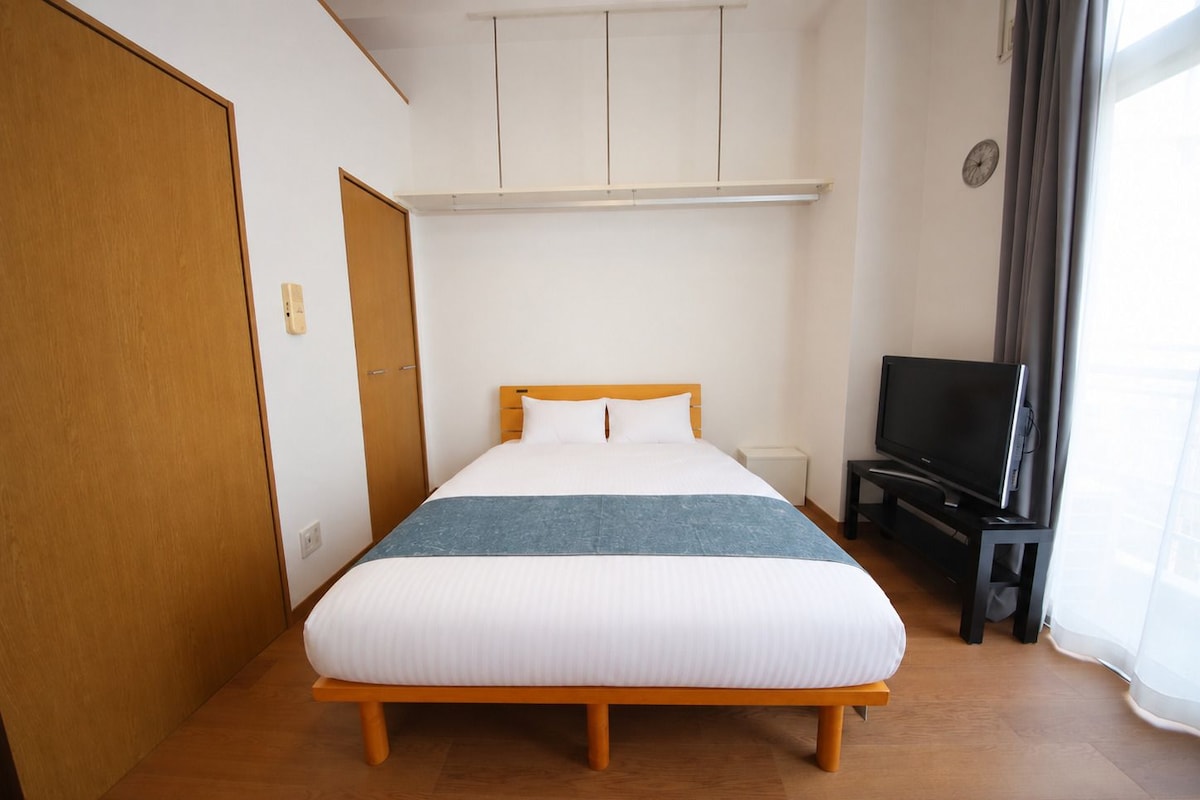 Ein Hotelzimmer mit Bett, Fernseher, Kleiderschrank und einem Fenster mit Vorhängen.