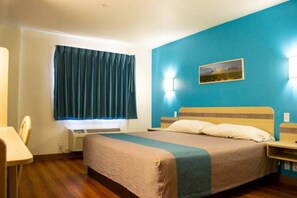 Une chambre d’hôtel comprenant un lit, un bureau, une chaise, une fenêtre avec des rideaux, un tableau accroché au mur et une table de chevet.