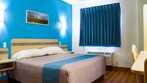 Quarto de hotel com cama, mesas de cabeceira, janela com cortinas e ar-condicionado fixado na parede.