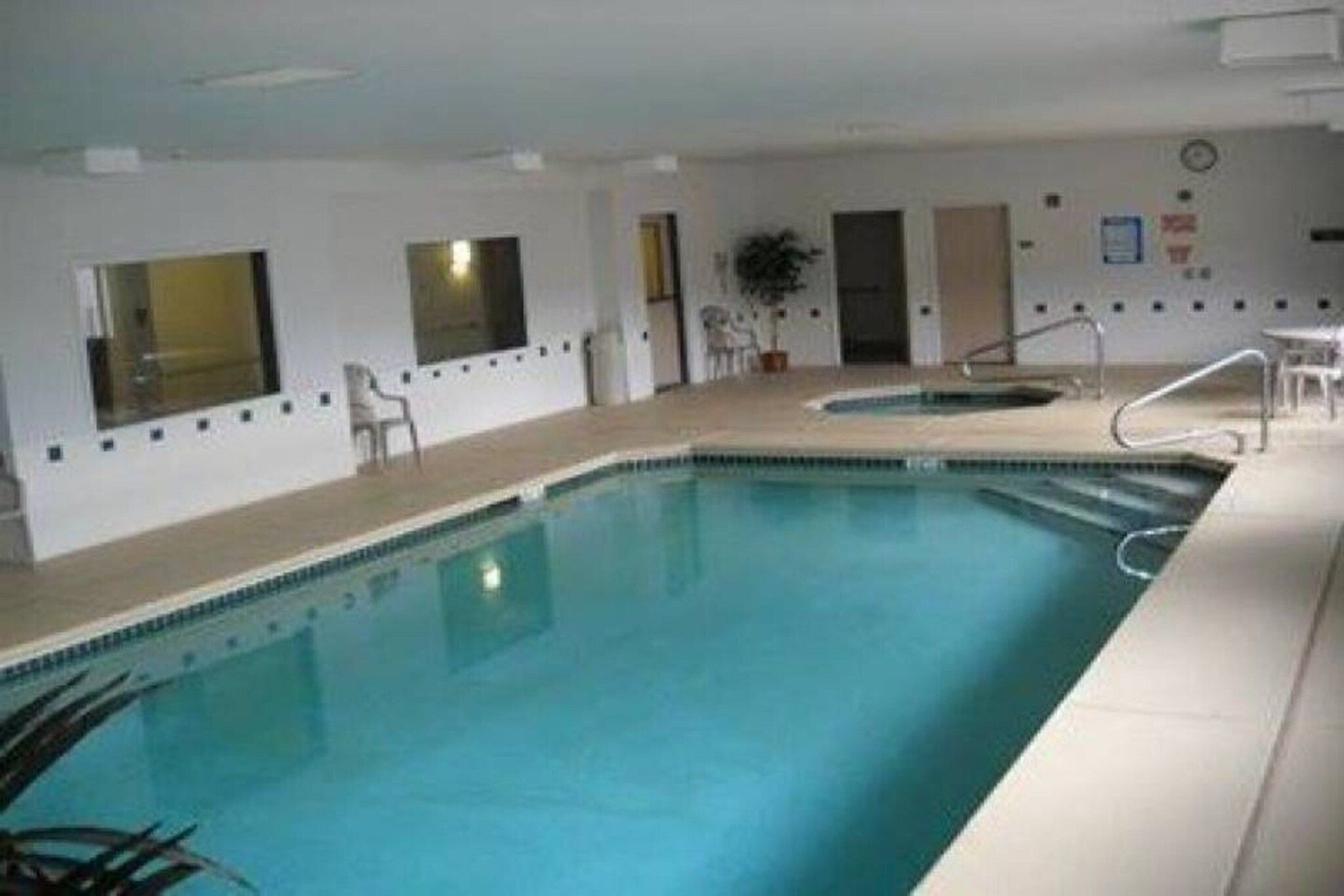 Une piscine intérieure à l’eau d’un bleu cristallin, dotée d’un plongeoir et d’un petit espace détente avec des chaises.