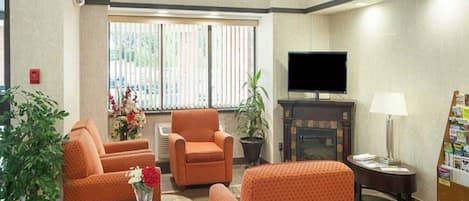 A hotel lounge with orange patterned sofas, a flat-screen TV, a fireplace, and a small table with a vase of flowers.
