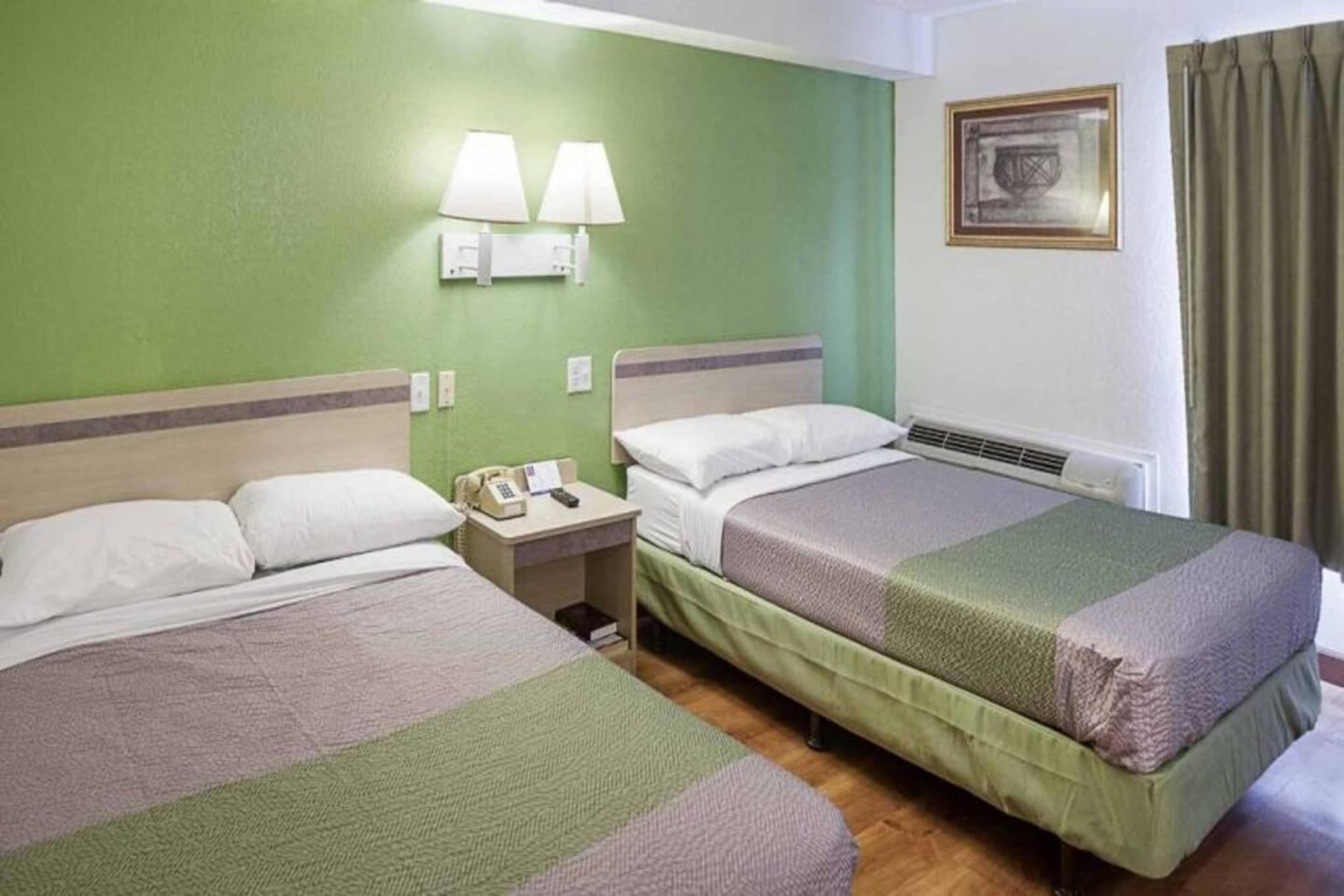 Habitación de hotel con dos camas, una mesita de noche con teléfono y una lámpara de pared.