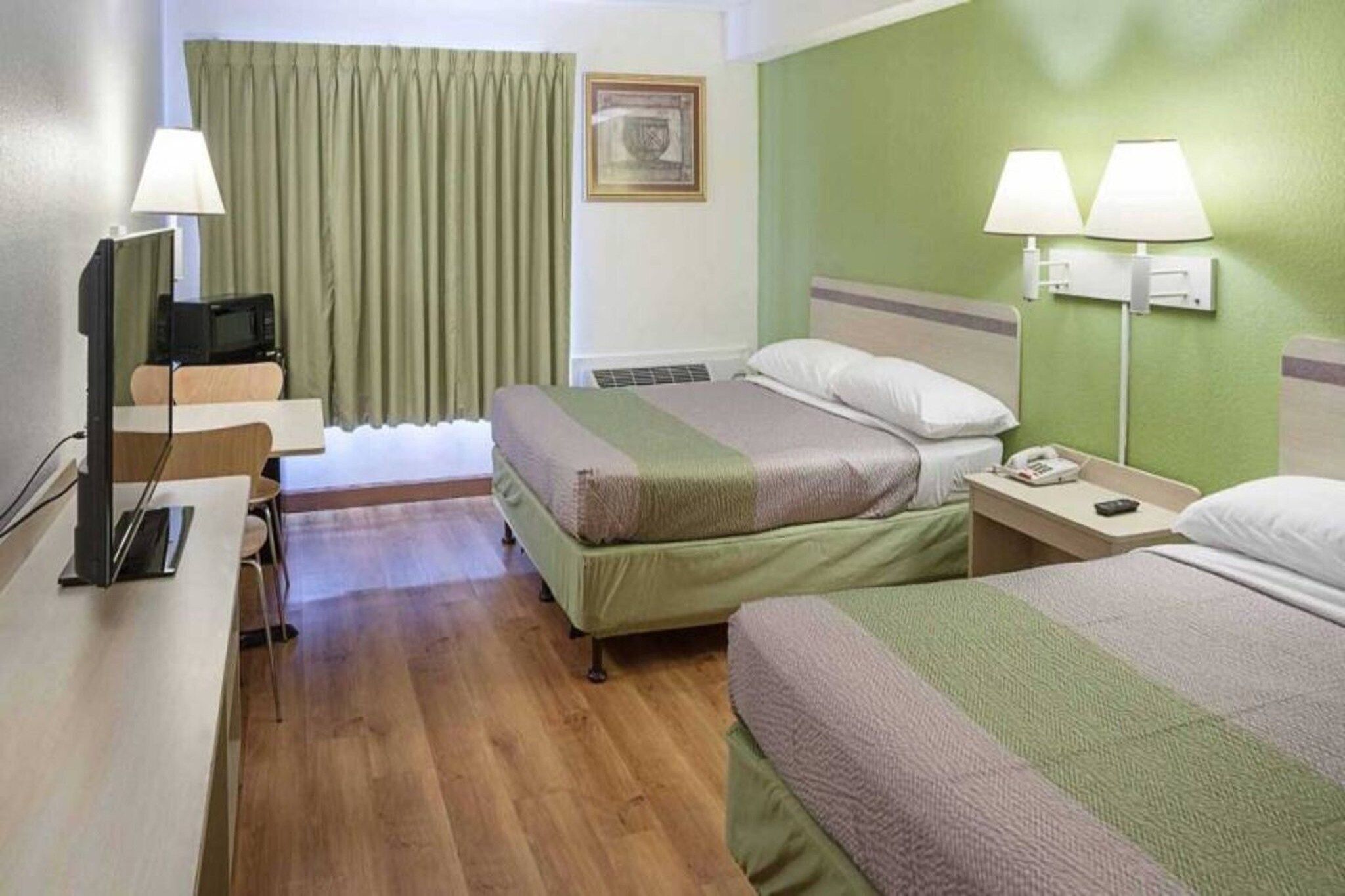 A hotel room with two beds, a desk with a computer, a chair, a television, and two bedside lamps.