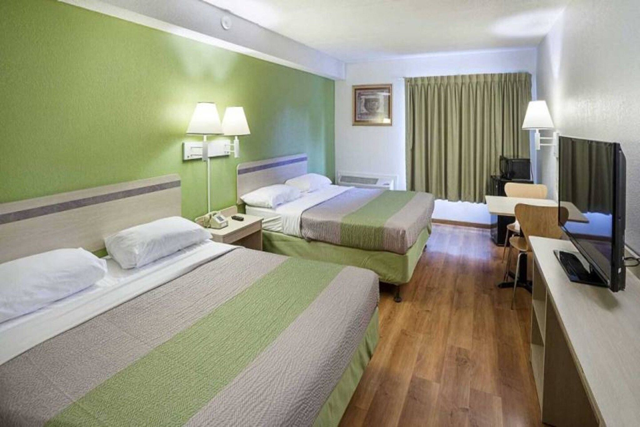 A hotel room with two beds, a desk, a television, and a window with curtains.