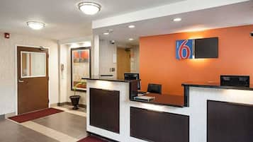 A hotel reception area with a reception desk, a number sign, a potted plant, and a red carpet.