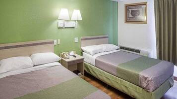 Habitación de hotel con dos camas, una mesita de noche con teléfono y una lámpara de pared.