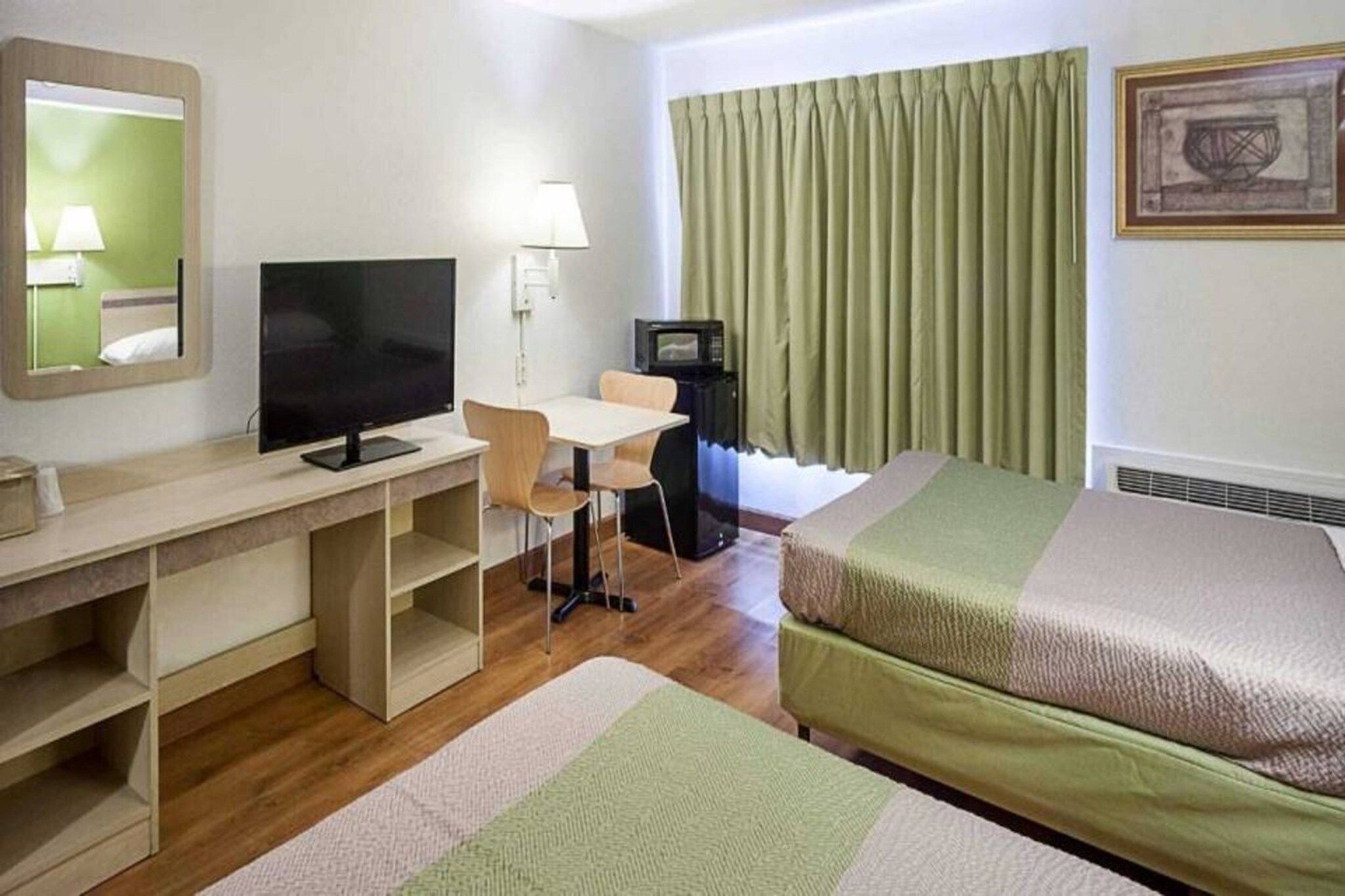 Ett hotellrum med ett skrivbord, en tv, en säng, en stol och ett fönster med gardiner.