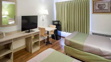 Quarto de hotel com escrivaninha, televisão, cama, cadeira e janela com cortinas.