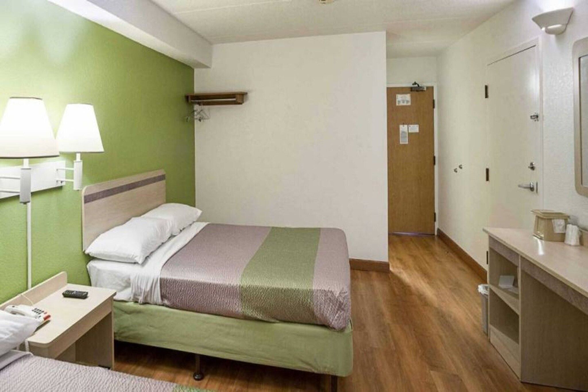 Een hotelkamer met een bed, nachtkastje, lamp en spiegel.