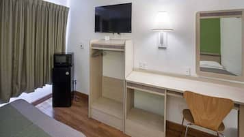 Quarto de hotel com cama, escrivaninha, cadeira, televisão, abajur e espelho.