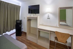 Una habitación de hotel con cama, escritorio, silla, televisor y microondas.