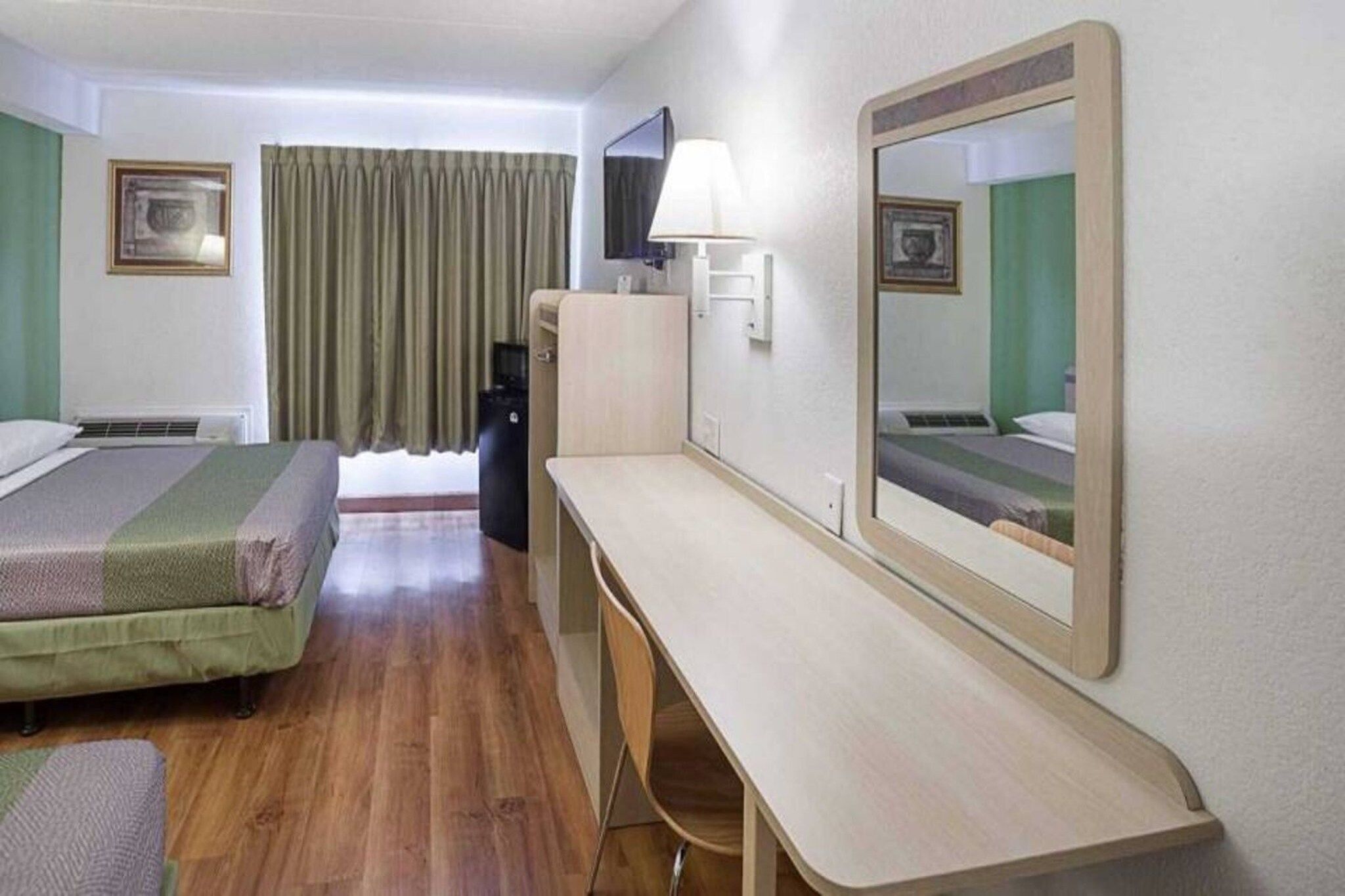 A hotel room with two beds, a desk, a chair, a television, and a mirror.