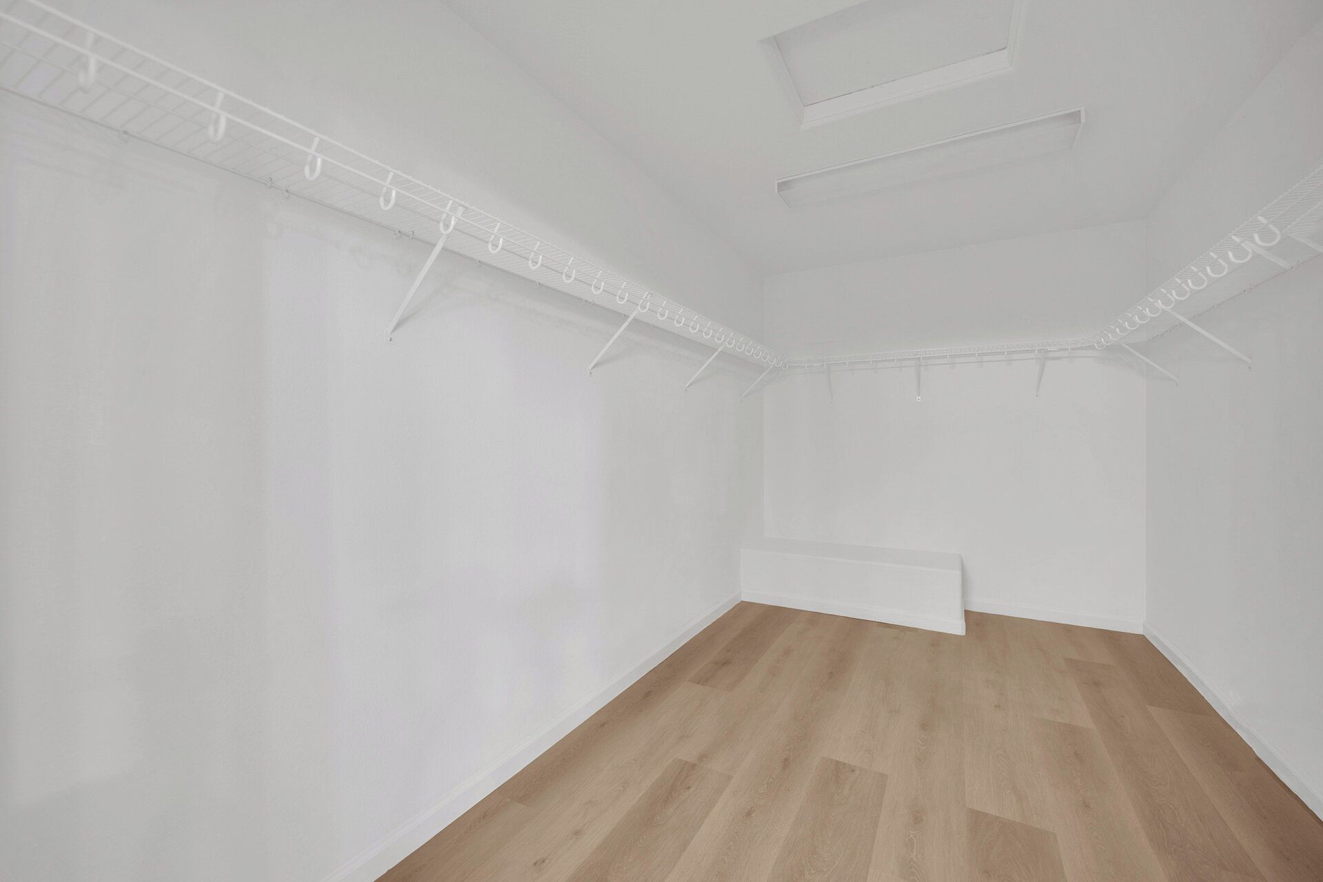 A room with white walls, a wooden floor, and a ceiling with a grid of lights.