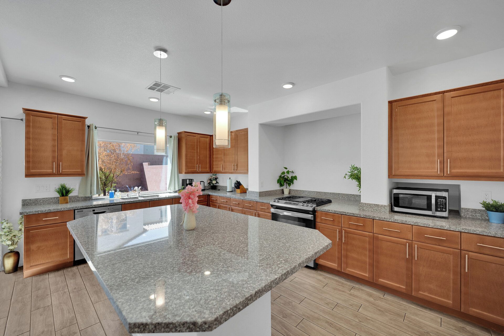 A modern kitchen with granite countertops, wooden cabinets, stainless steel appliances, and pendant lighting.