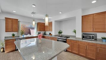A modern kitchen with granite countertops, wooden cabinets, stainless steel appliances, and pendant lighting.