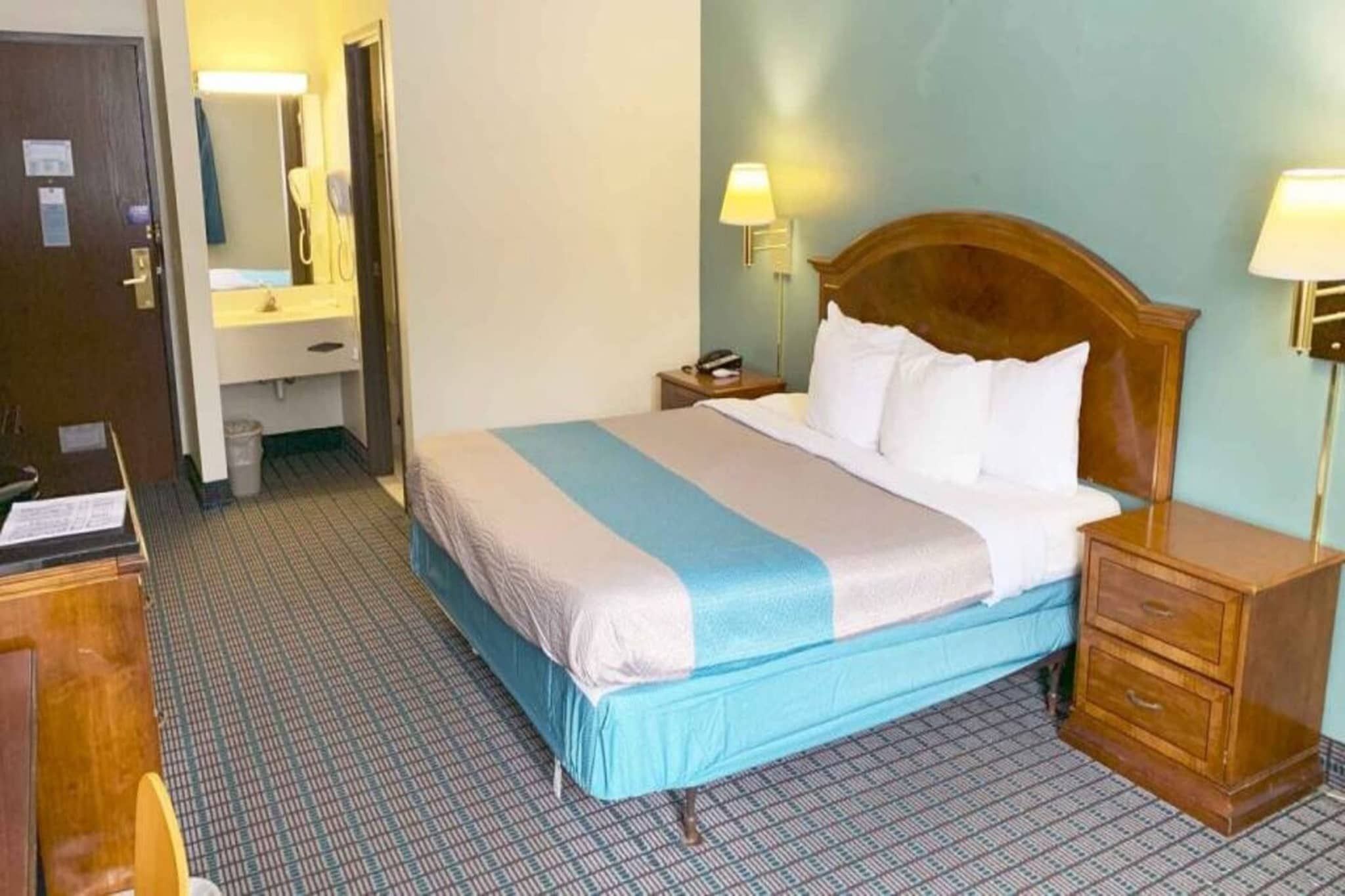 A hotel room with a bed, bedside tables, a nightstand, a mirror, and a bathroom.