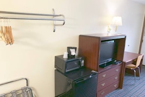 Ein kompaktes Hotelzimmer mit einer Küchenzeile, einer Mikrowelle, einem kleinen Kühlschrank, einer Holzkabine mit einem Fernseher, einem Sessel und einer Lampe.
