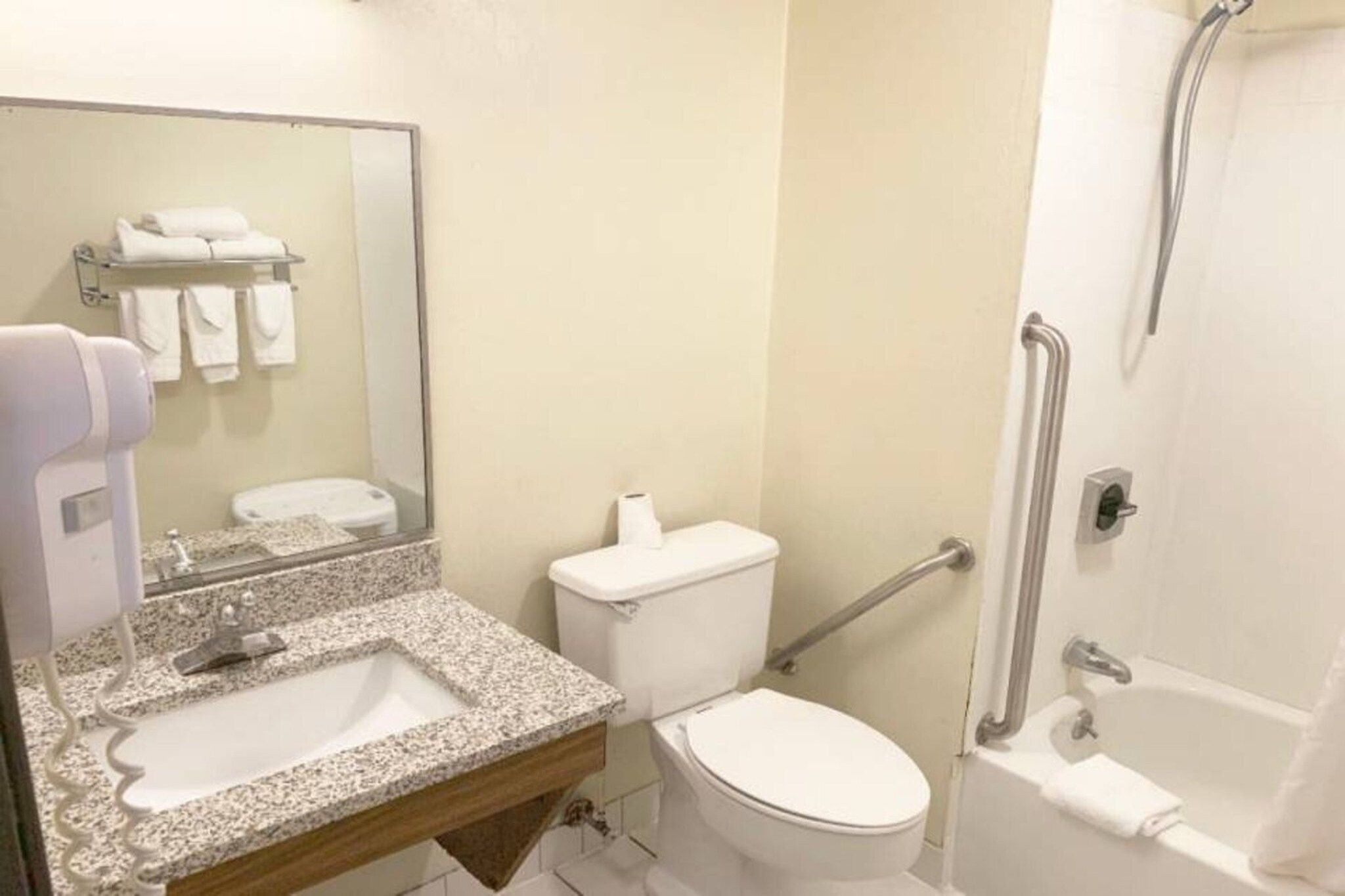 Badeværelse med granitbordplade, håndvask, toilet, brusebad med gelænder og et spejl med håndklæderække.