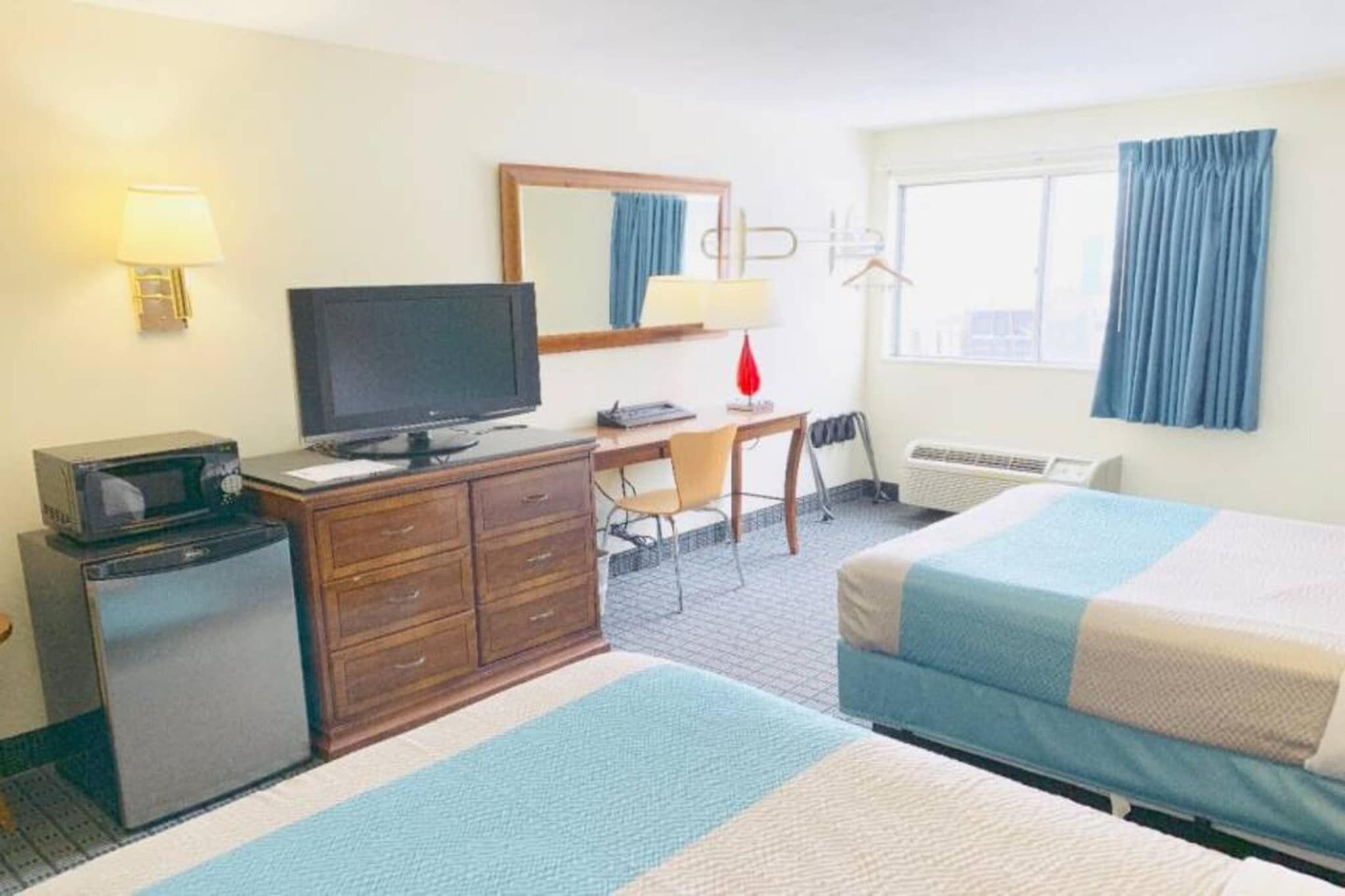 A hotel room with a bed, a desk with a computer, a television, a dresser, and a window with curtains.