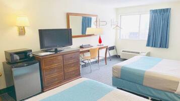 A hotel room with a bed, a desk with a computer, a television, a dresser, and a window with curtains.