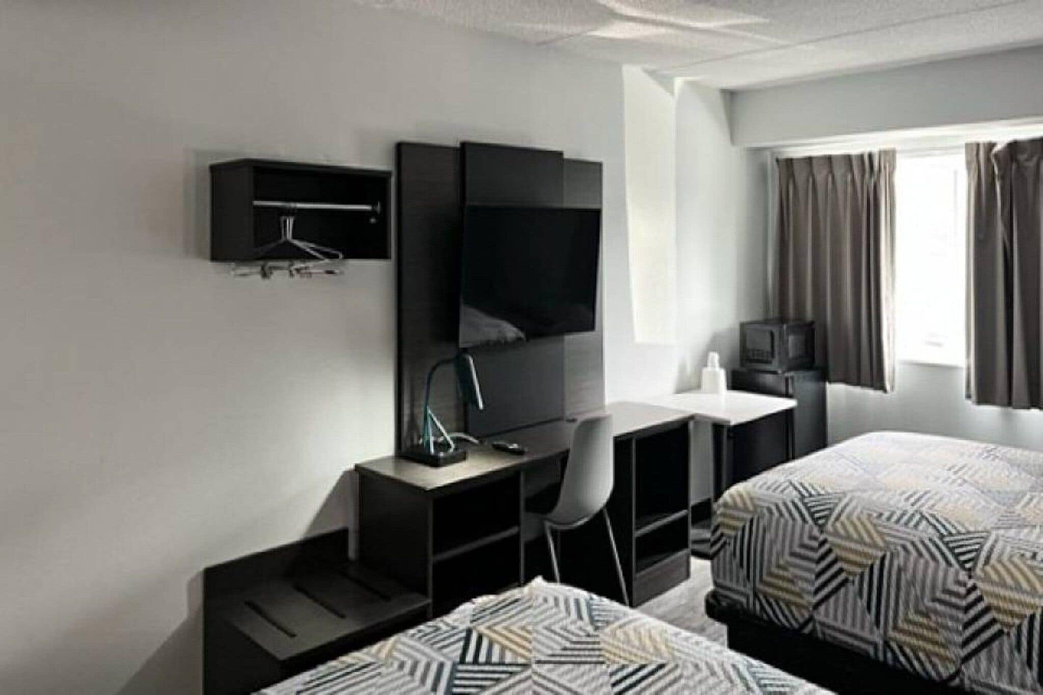 A hotel room with two beds, a desk, a chair, a TV, and a window with curtains.