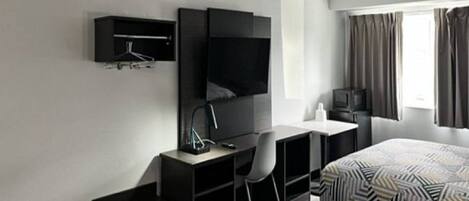 A hotel room with two beds, a desk, a chair, a TV, and a window with curtains.