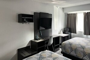 A hotel room with two beds, a desk, a chair, a TV, and a window with curtains. - 1 King Bed | Suite, Non-Smoking, Micfridge (East Syracuse)