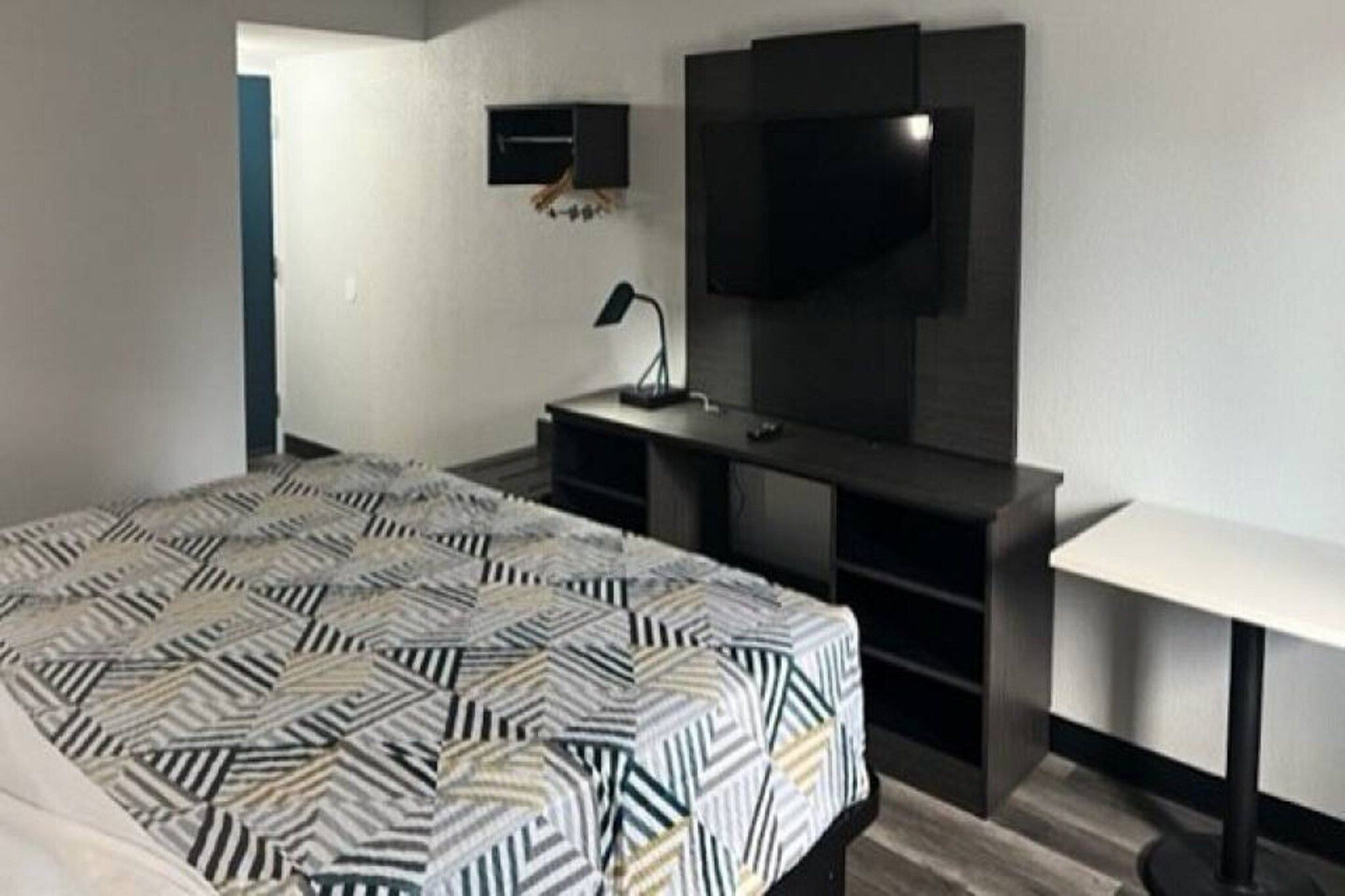 Un dormitorio con cama, escritorio, silla, televisor y lámpara.