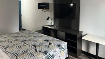 Un dormitorio con cama, escritorio, silla, televisor y lámpara.