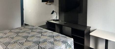A bedroom with a bed, a desk, a chair, a TV, and a lamp.