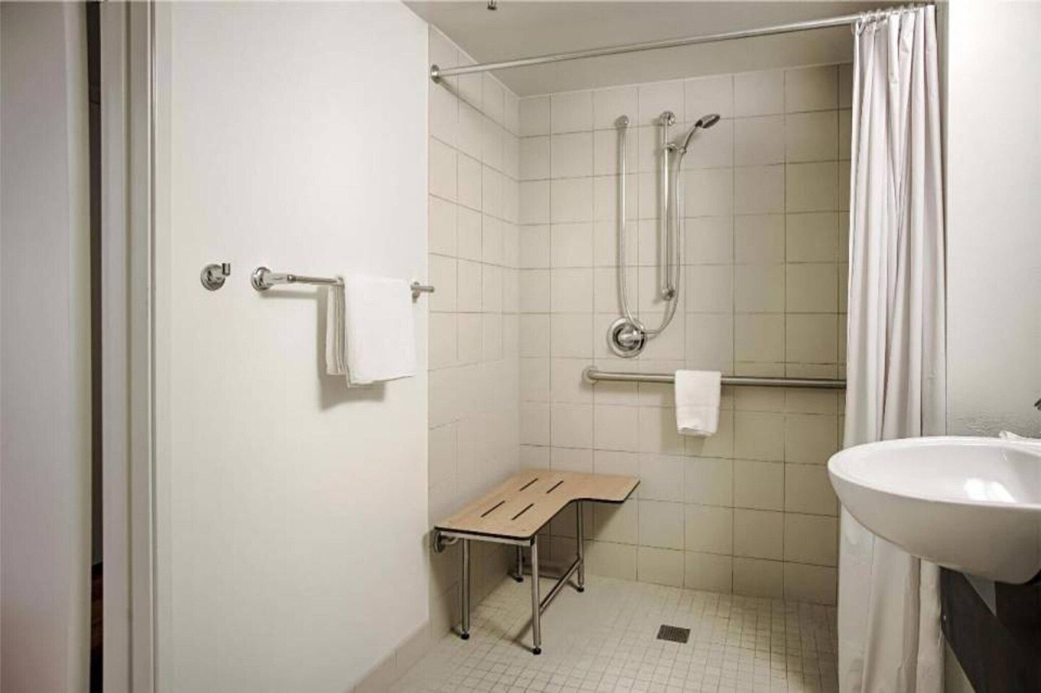 Un baño con ducha, lavamanos y una mesita.