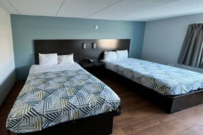 Habitación de hotel con dos camas, cada una con ropa de cama estampada, una mesita de noche y una lámpara fijada a la pared.